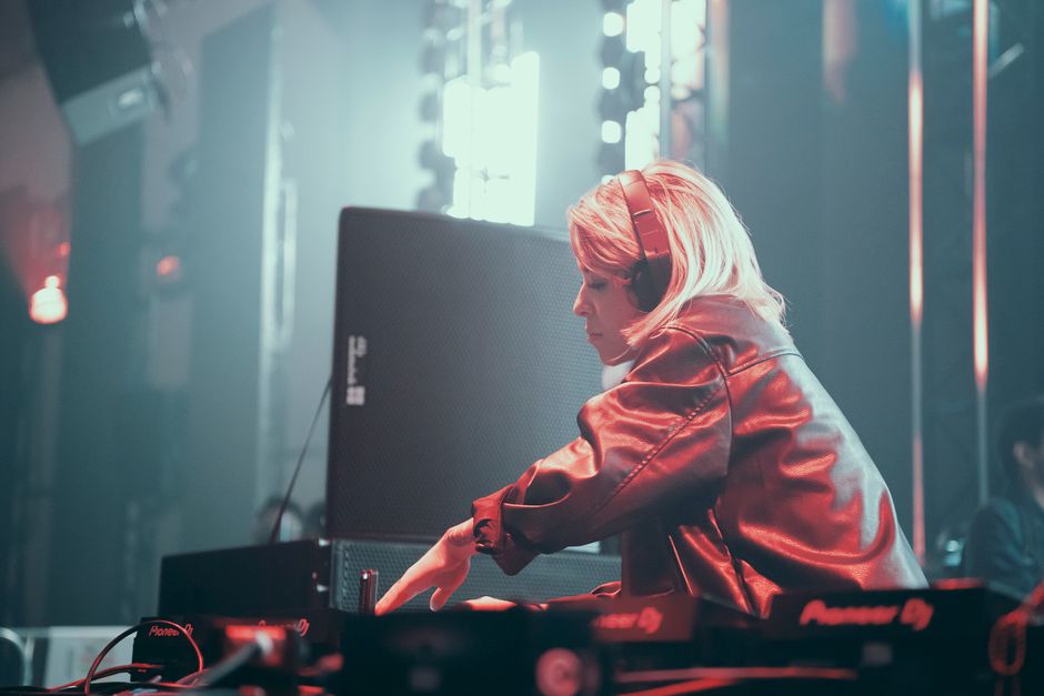 DJ wearing headphones mixing music on console at lively night club.